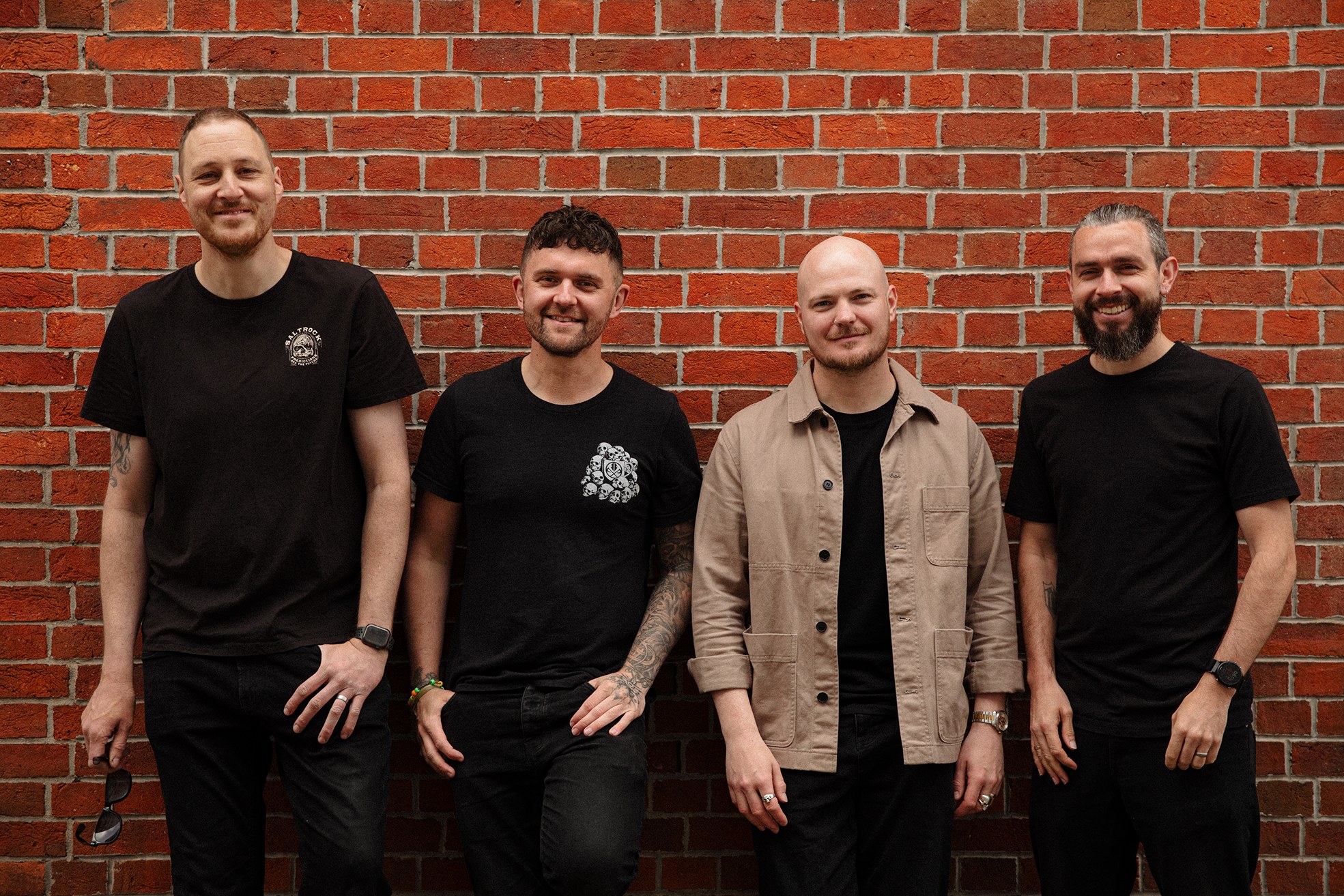 The four members of Ironhide leaning against a red brick wall, smiling