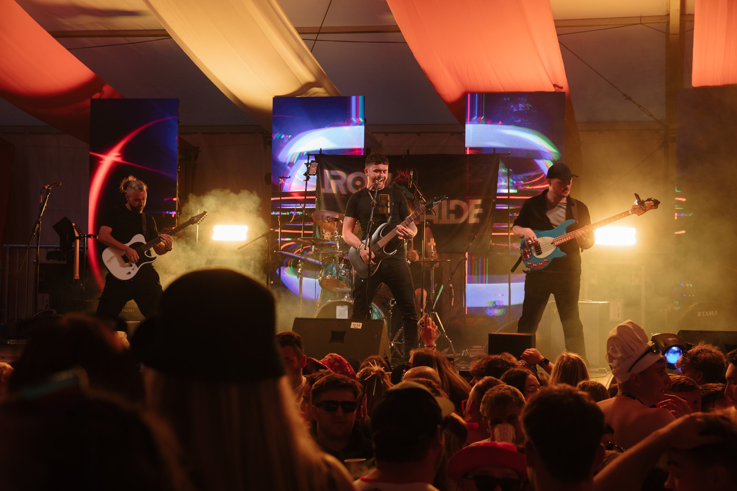 Ironhide on stage in a festival tent, amber light and haze, crowd in front